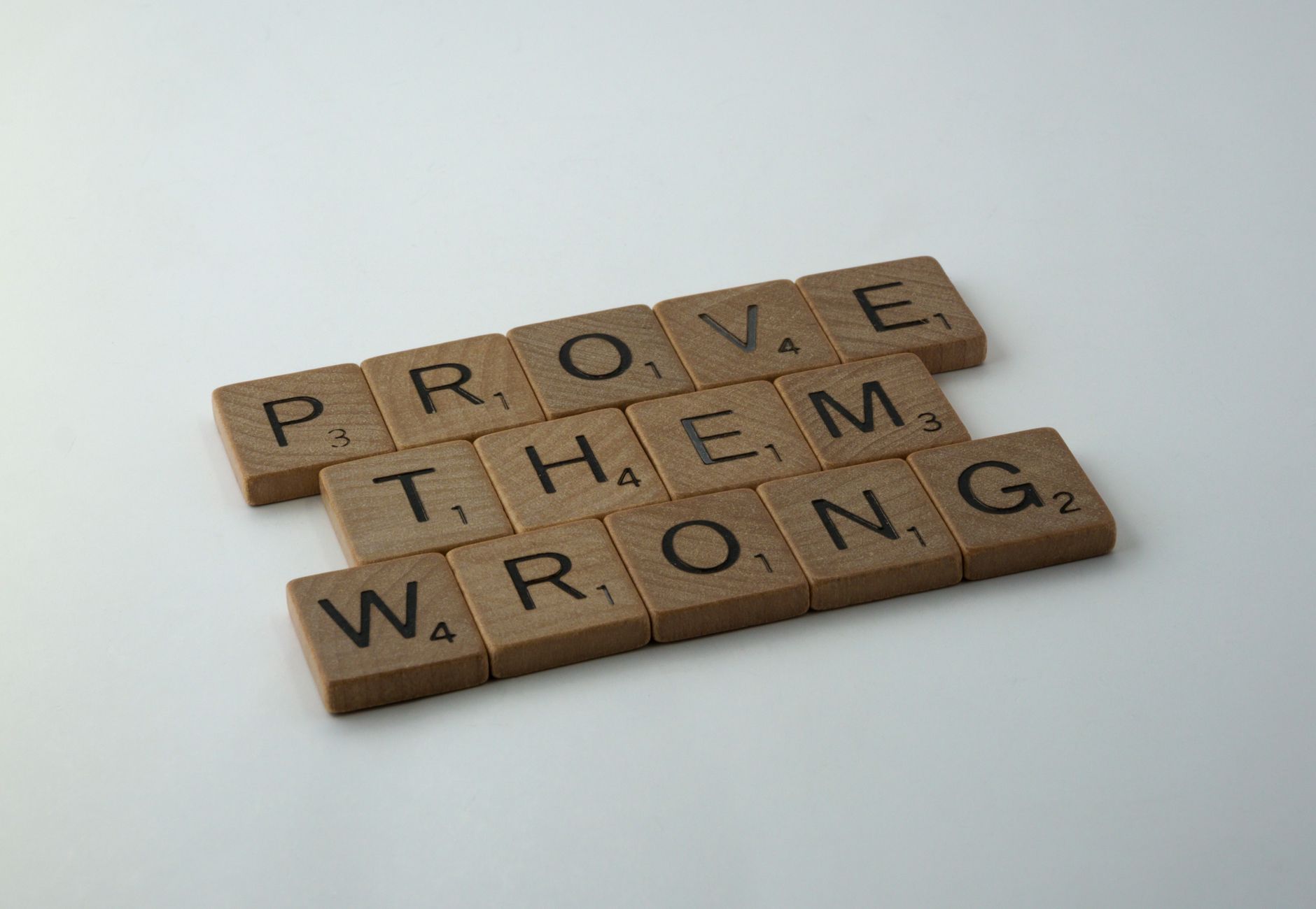 Scrabble tiles spelling the motivational phrase 'Prove Them Wrong' on a neutral background.