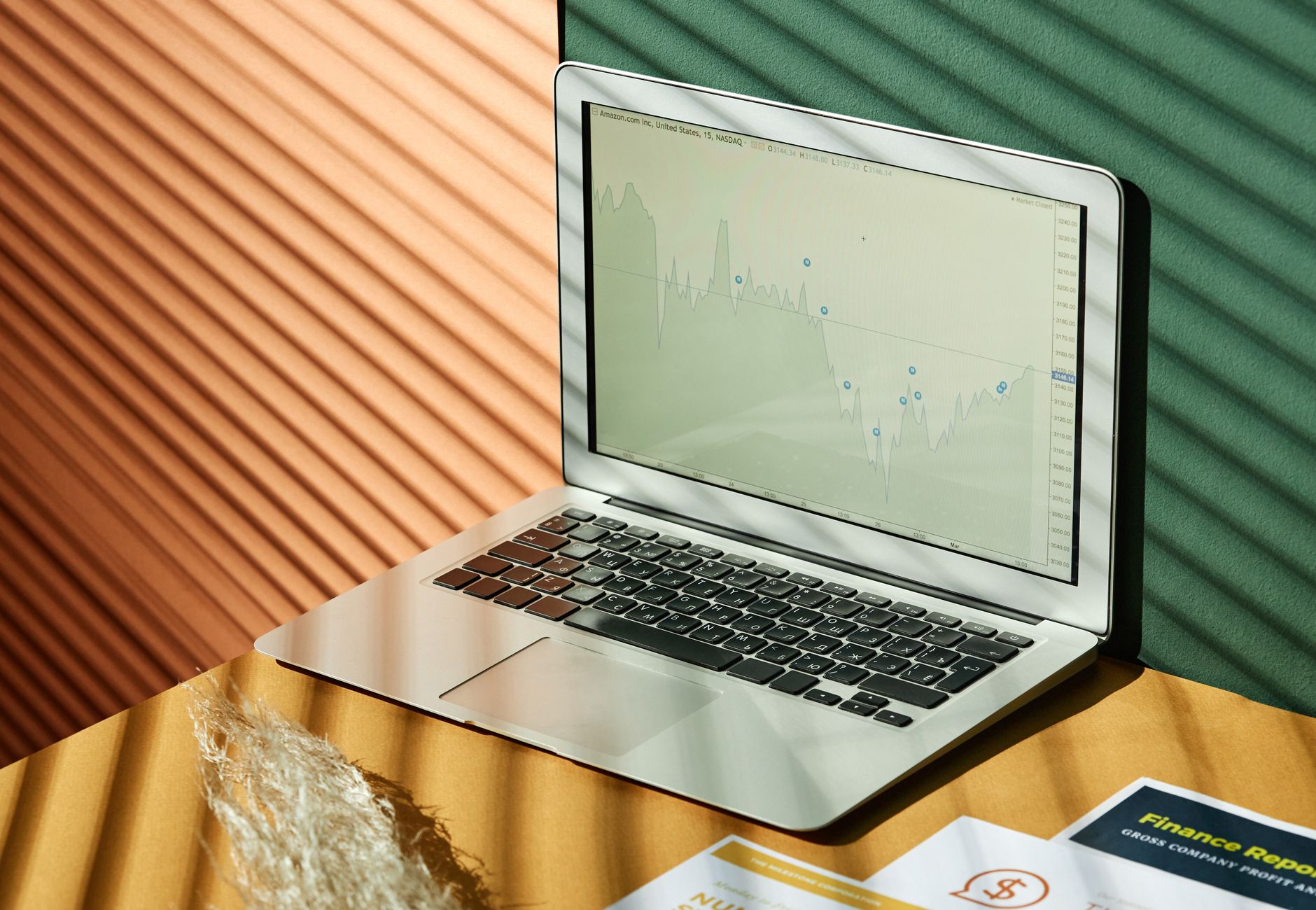 A laptop displaying analytics with financial papers on a textured surface, captured in warm lighting.