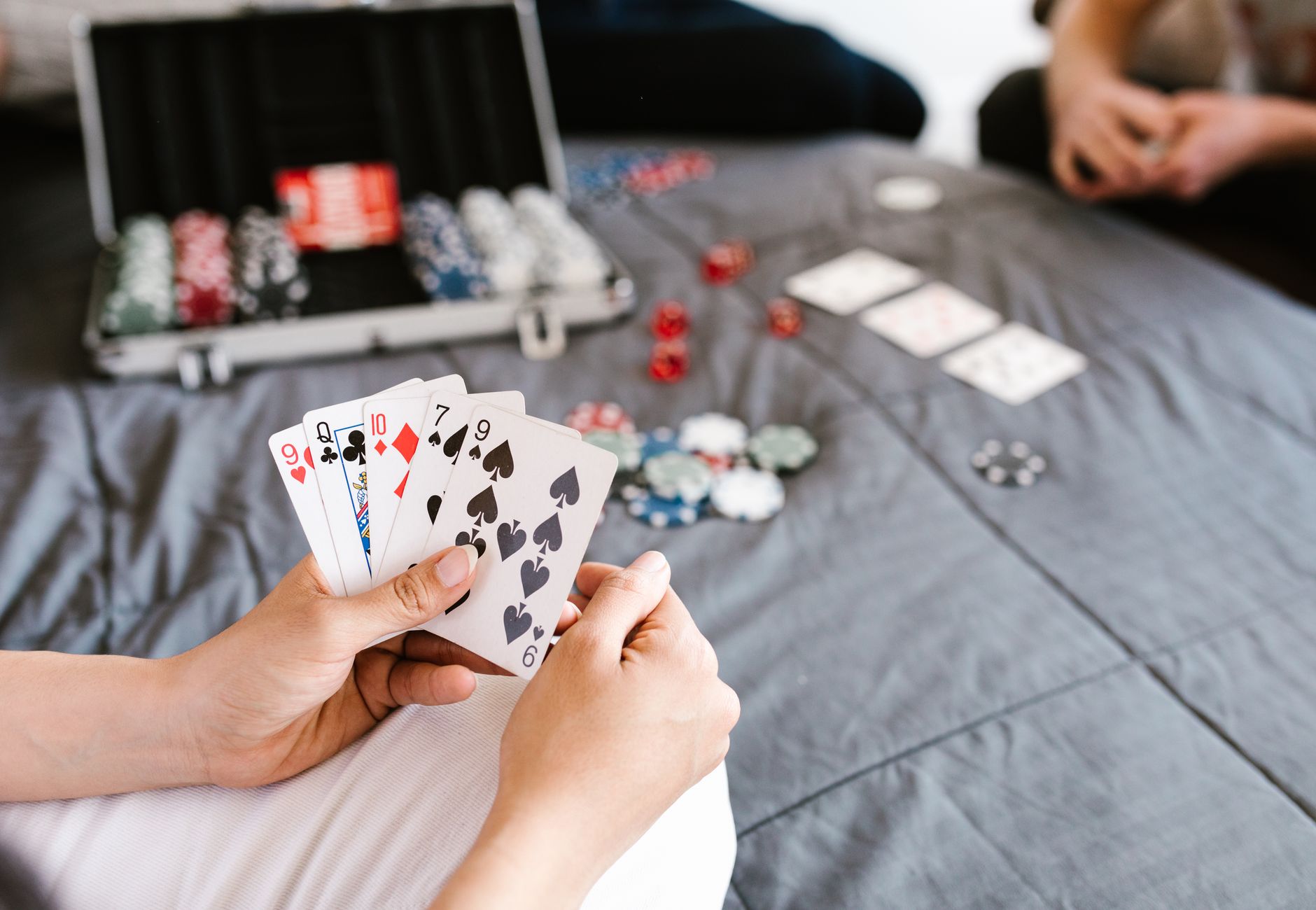 Close-up of a poker game with playing cards and chips on a table. Focus on player's hand.